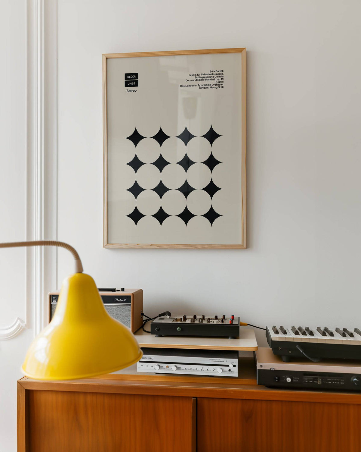 Graphic Art Poster framed print with black star shapes in minimalist style above a wooden sideboard in a music room
