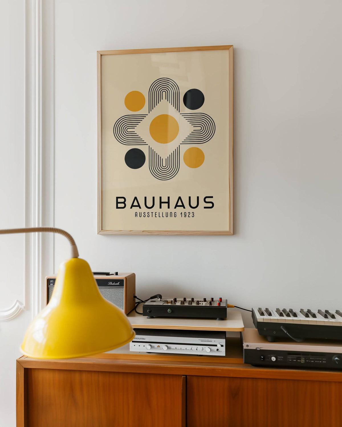 Geometric Abstract wall art of bauhaus shapes in mustard and black above audio equipment with yellow lamp