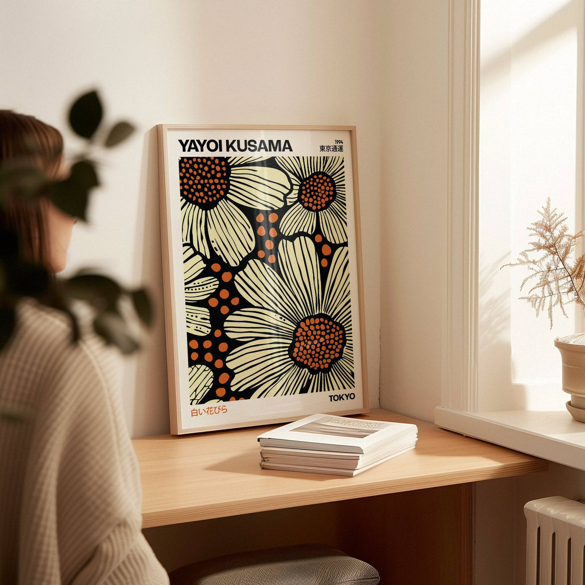 Print leaning on a table of stylised daisies with orange and cream on black near a pot plant