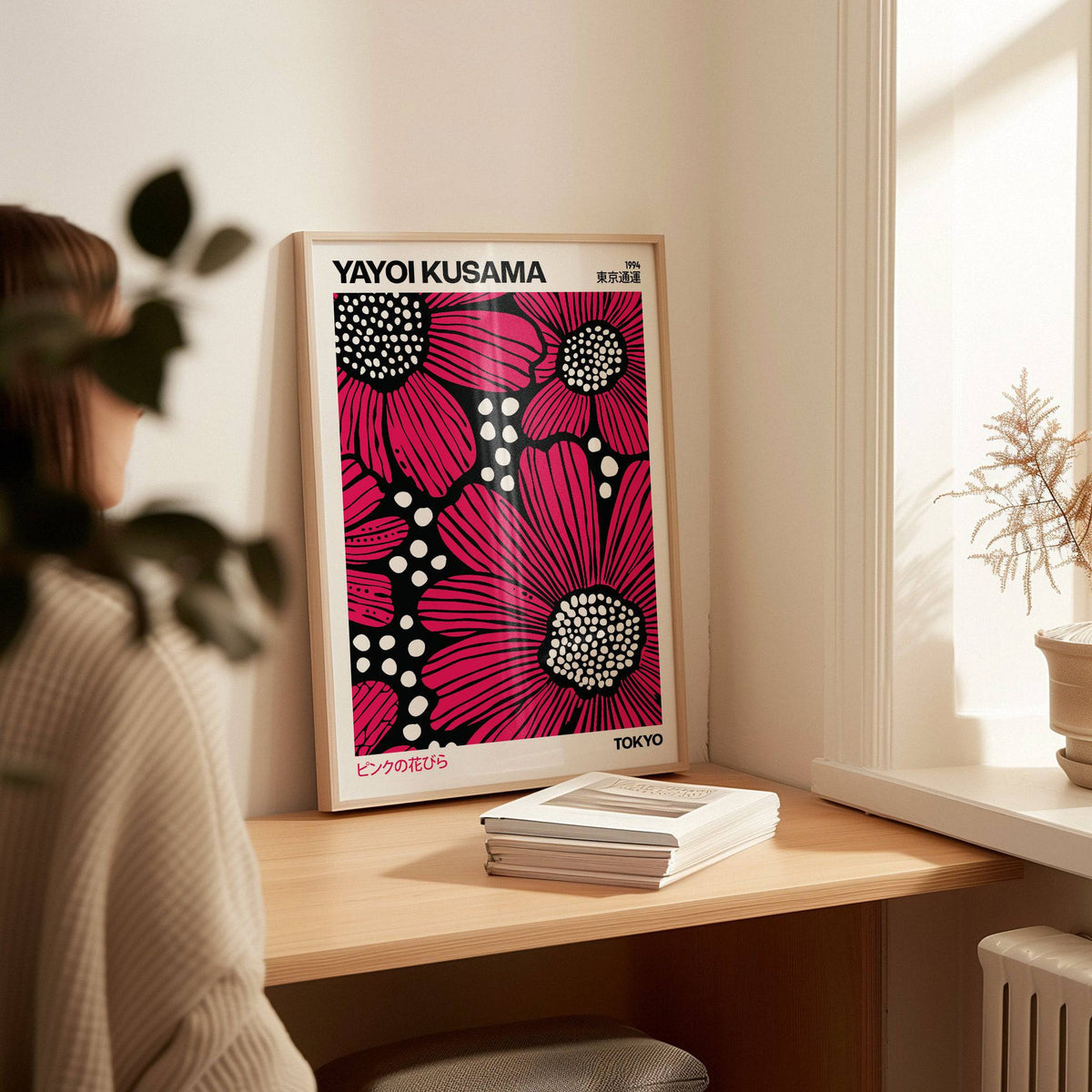 Print leaning on a desk Pink Posters with red daisies and black and white spots in a bright room with plant