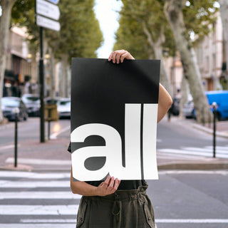 Person holding typography art print with large white text all on black background on outdoor street