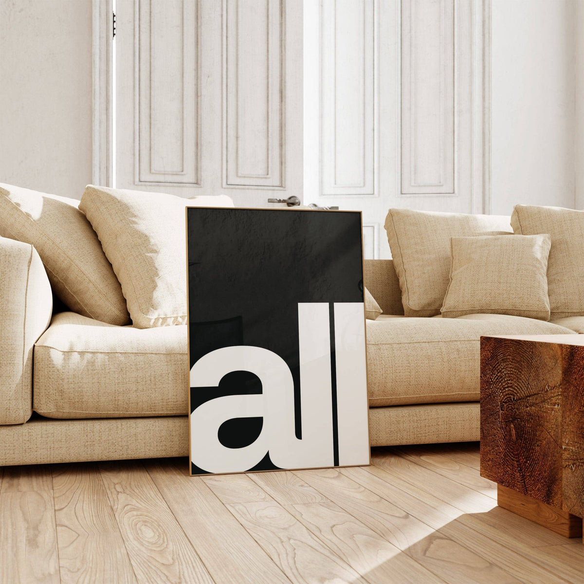 Print leaning on a floor with black background and large white bold typography 'all' near a beige sofa