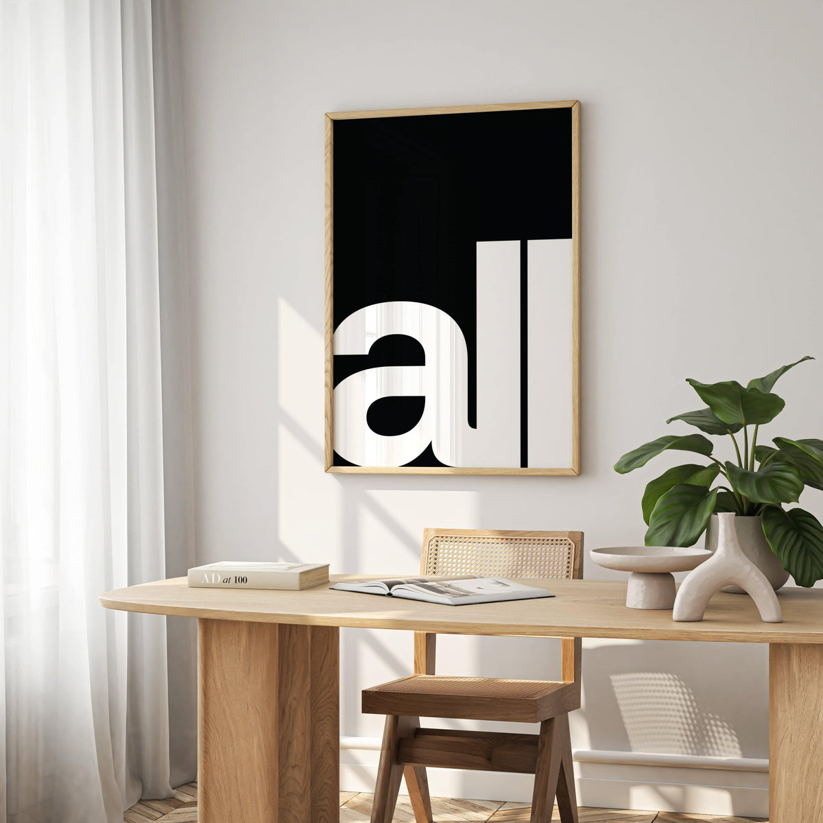 Typography art prints of minimalist white text on black background in a bright dining area with light wooden table and plant