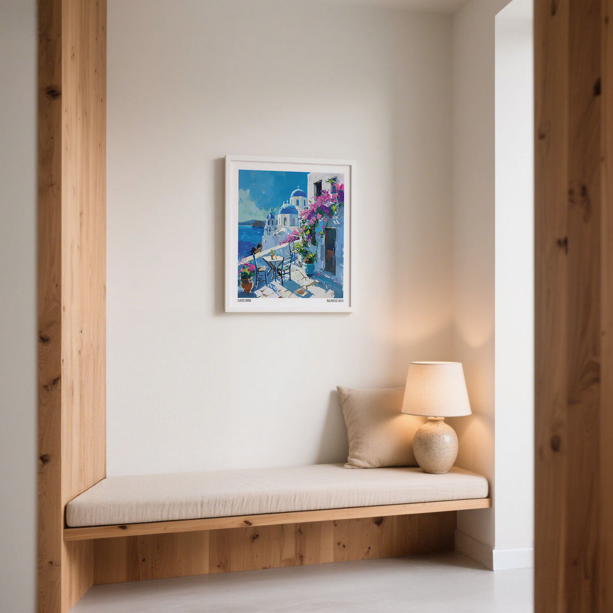 Santorini wall art prints above a beige cushioned bench and lamp in a bright nook