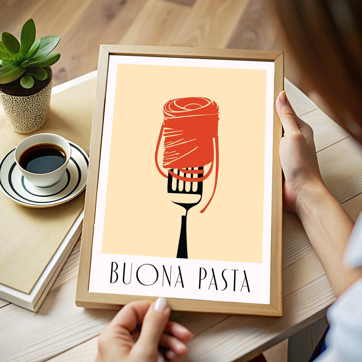 Framed Buona Pasta print of pasta on a fork with typographic text held above a table with a cup of coffee