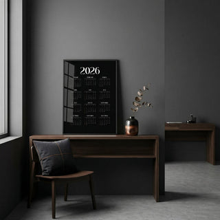 Modern Calendar Print leaning on a desk with a dark wall and a vase with dried leaves