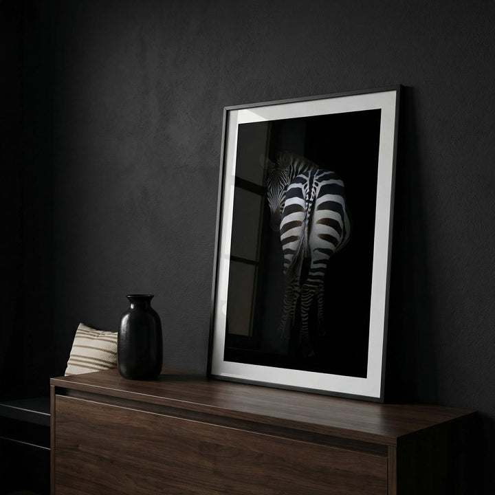 Framed zebra art print with rear view of a zebra on a dark background on a wooden sideboard with a black vase