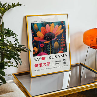 Framed flower wall decor with an orange flower and botanical illustration style leaning on a glass table beside a green plant