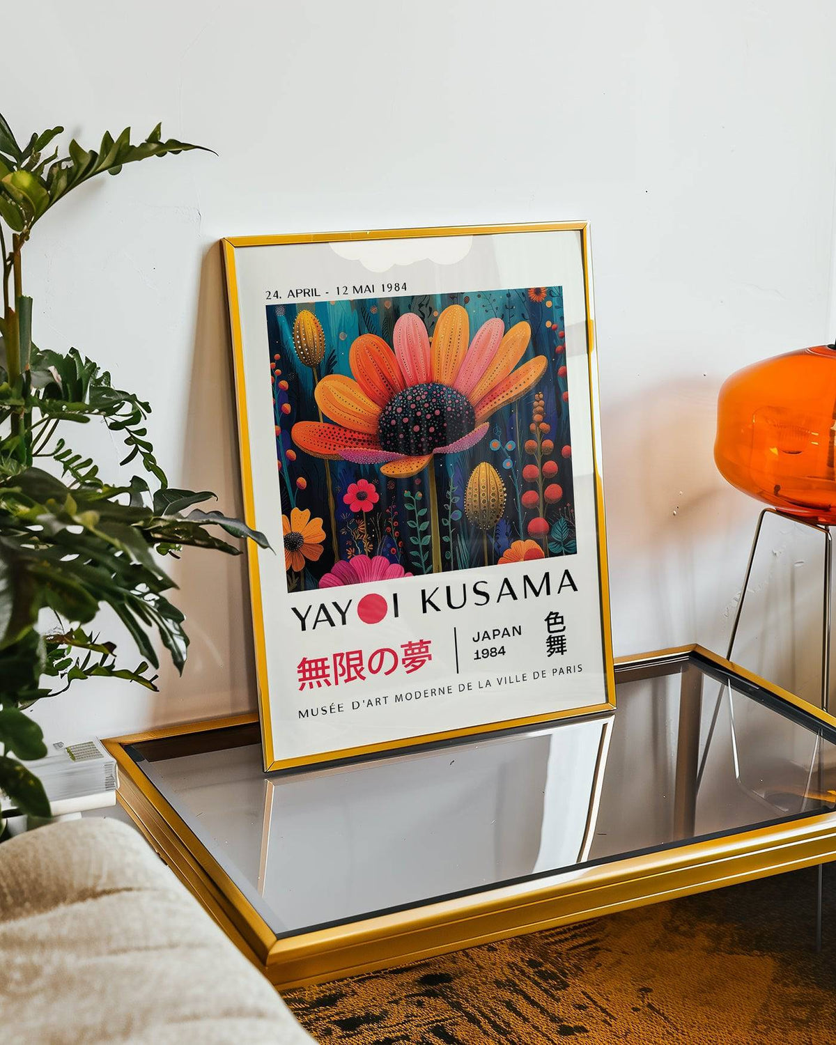 Framed flower wall decor with an orange flower and botanical illustration style leaning on a glass table beside a green plant