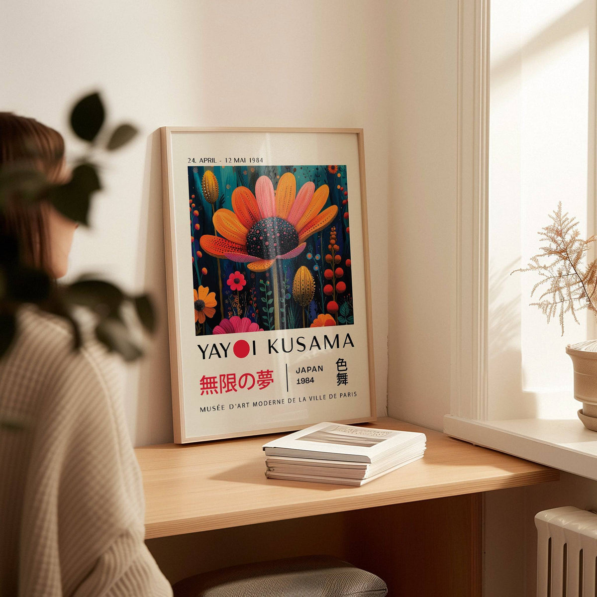 Flower wall decor print leaning on a wooden desk with books and a potted plant