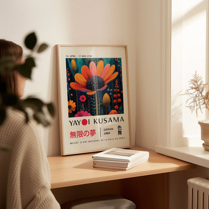 Flower wall decor print leaning on a wooden desk with books and a potted plant