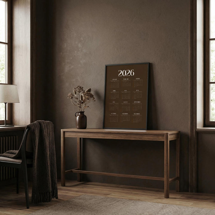 Brown Calendar Print leaning on a wooden table with a brown vase and dried flowers in a brown room