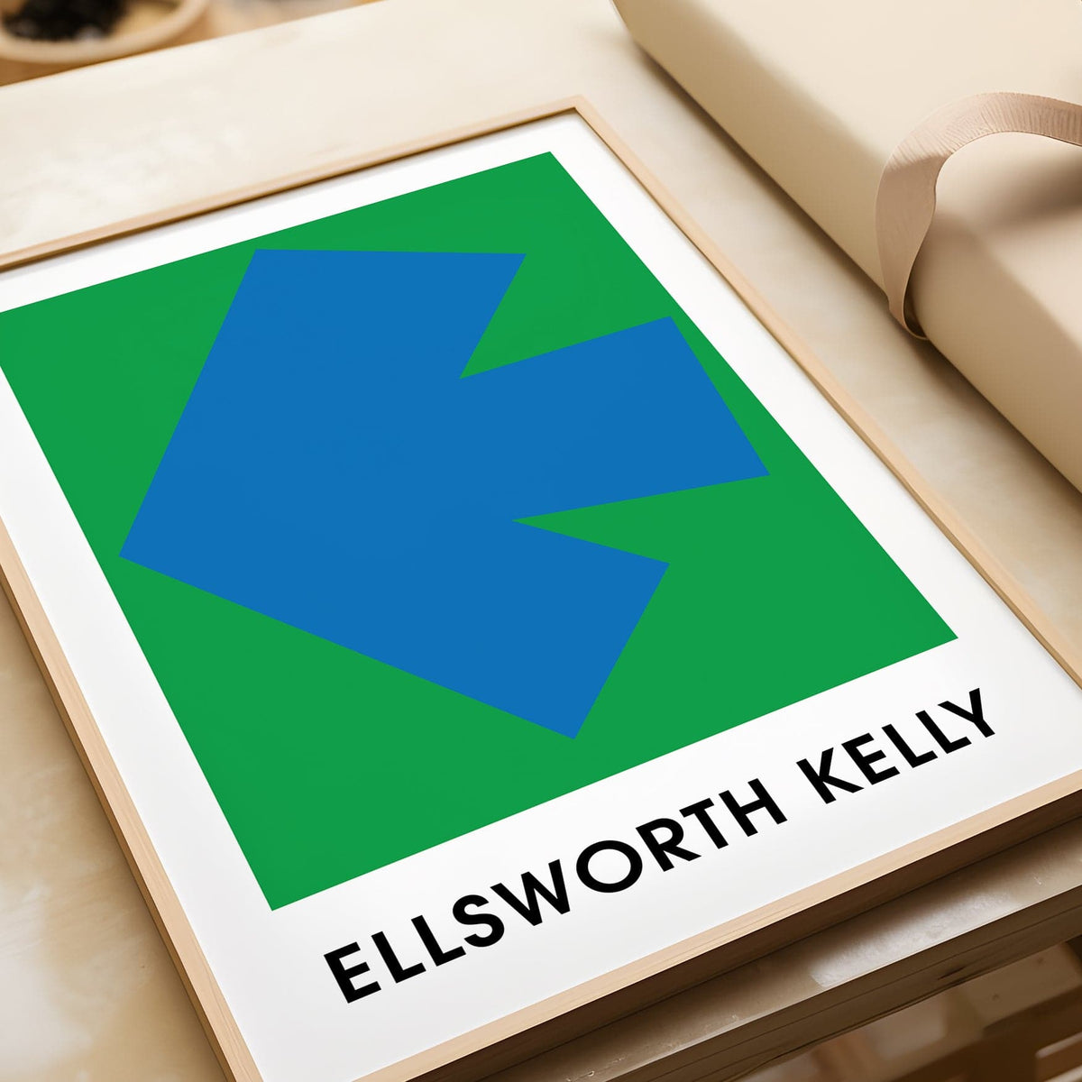 Framed Ellsworth Kelly art print with a blue arrow on a green background on a marble surface beside beige wrapping paper