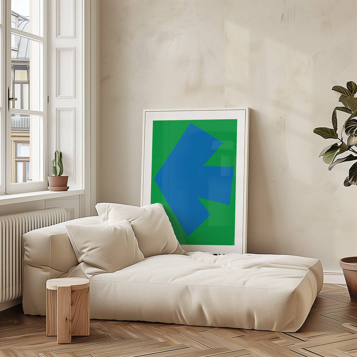 Ellsworth Kelly art print with a blue arrow shape on green background leaning against a beige wall above a cream sofa