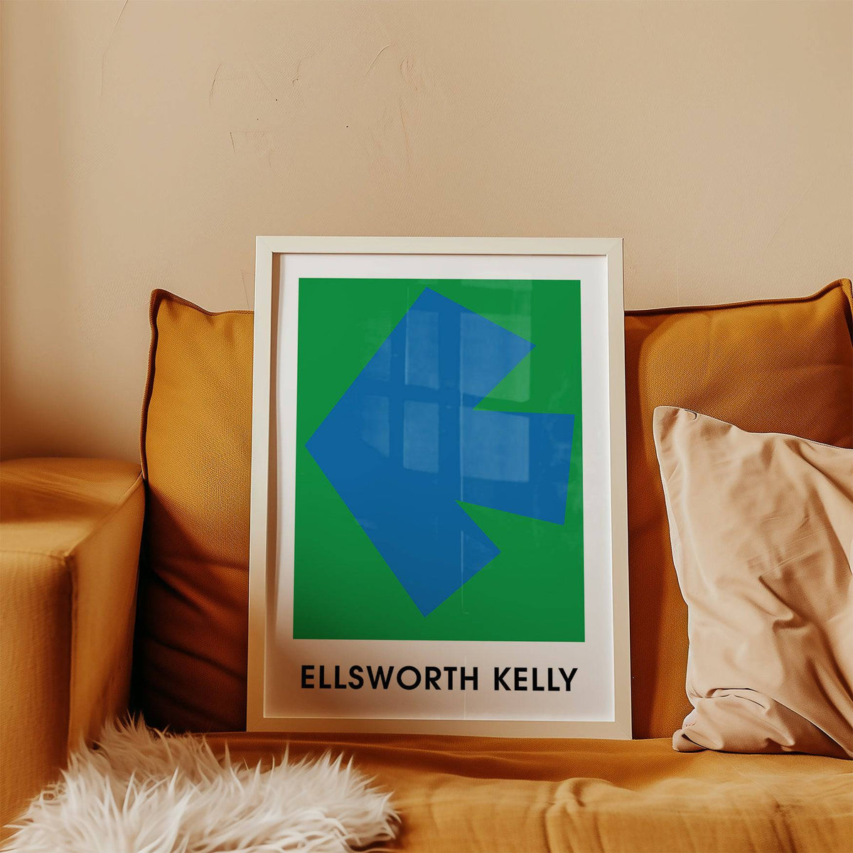 Framed Ellsworth Kelly art print with blue arrow shape on green leaning on mustard sofa with cushions