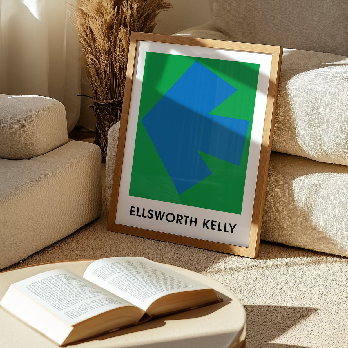Framed Ellsworth Kelly Art Print with a blue arrow on green leaning by a beige sofa and book