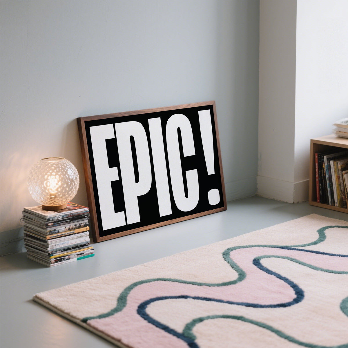 Print leaning on floor with bold white EPIC text on black background near glass lamp on stack of books