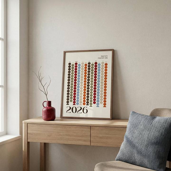 Big Calendar for Wall leaning on a wooden desk with a red vase and a knitted cushion nearby