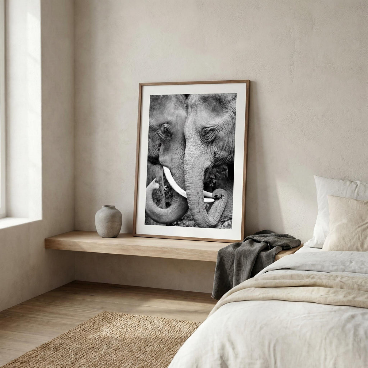 Print leaning on a shelf of two elephants touching trunks in black and white with a grey vase nearby in a bedroom