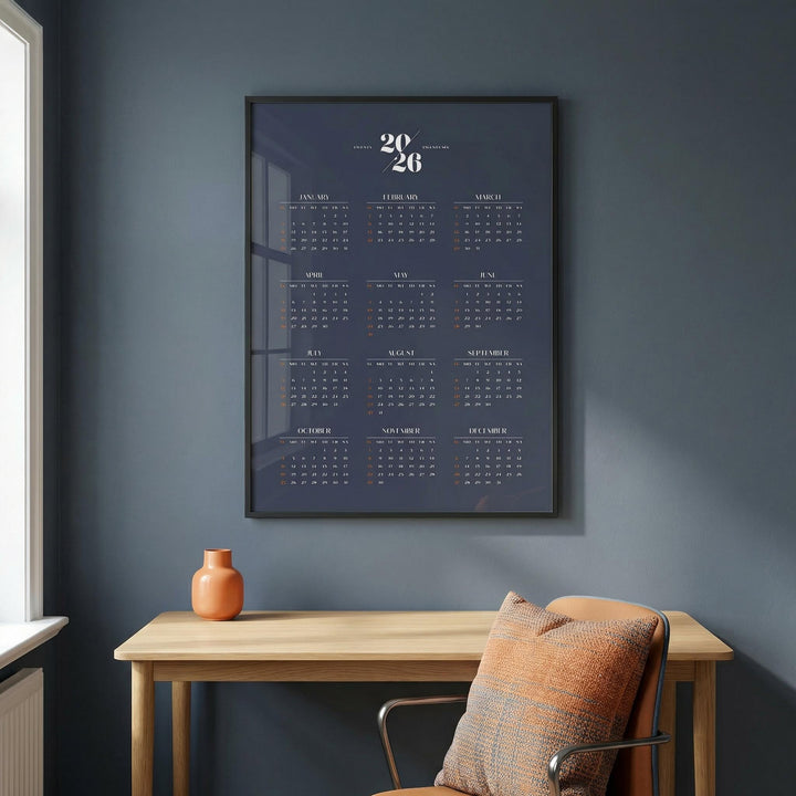 Minimalist Calendar as framed print on a dark grey wall above a wooden table with a terracotta vase and an orange cushion