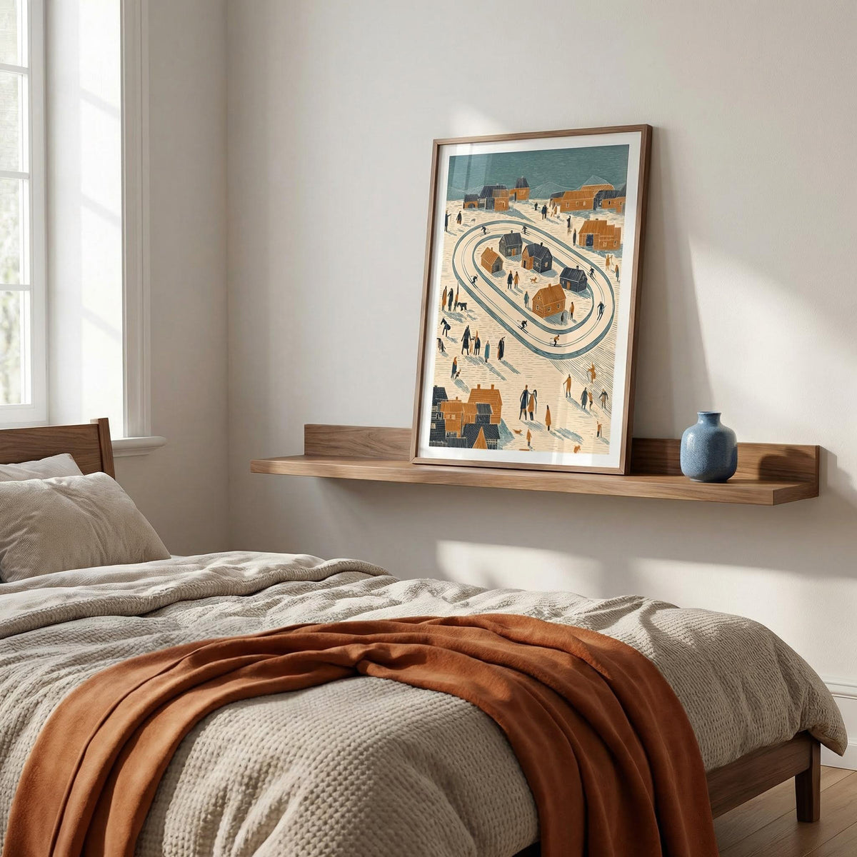 Winter Village Art Print leaning on a wooden shelf with a blue vase by a bed with rust and beige bedding