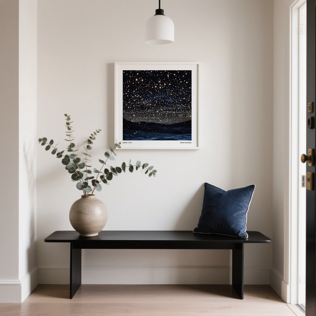 Starry Night Print framed on a white wall above a black bench with a blue cushion and a vase with eucalyptus