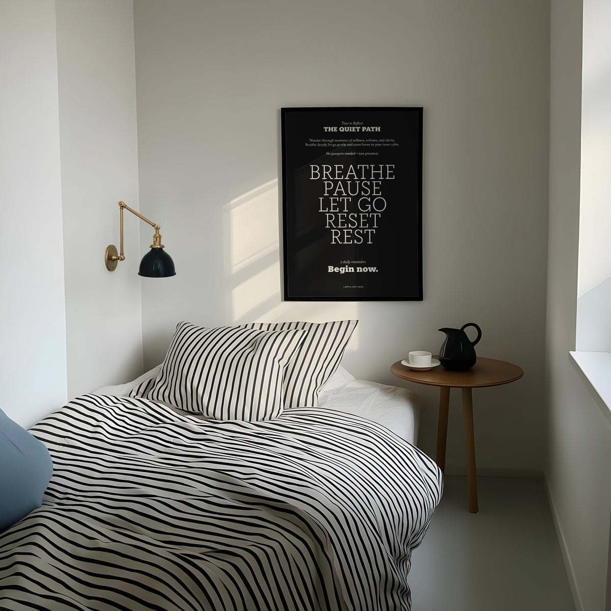 Meditation wall art with motivational text in black and white above a wooden bedside table with a jug and cup in a minimal bedroom
