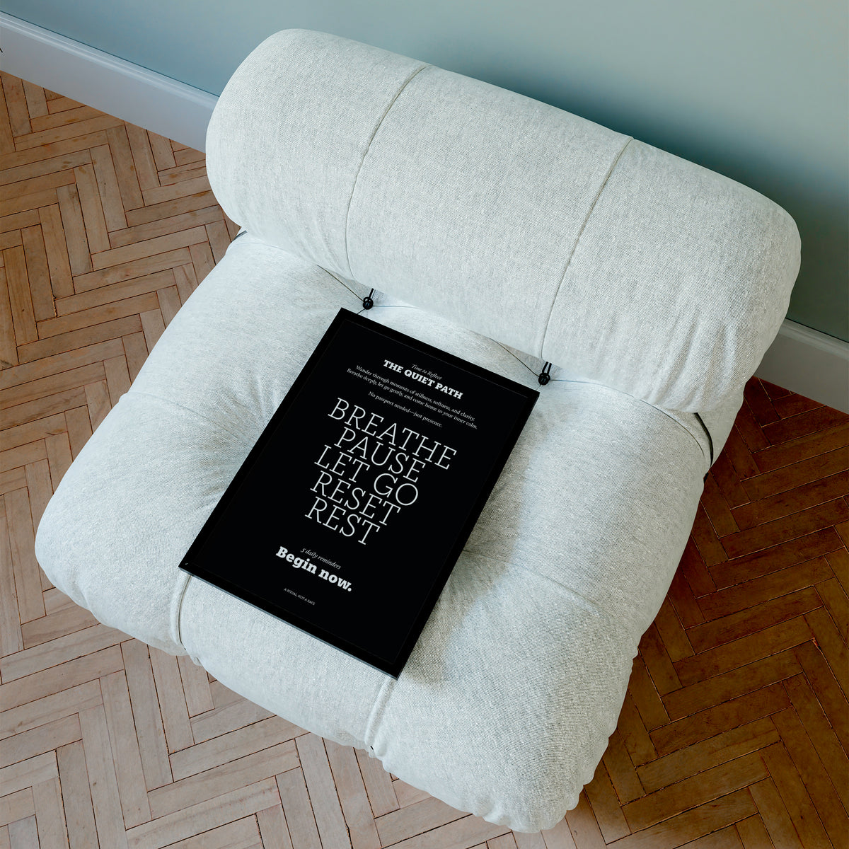 Meditation wall art with white typographic motivational text on black leaning on a beige cushioned chair