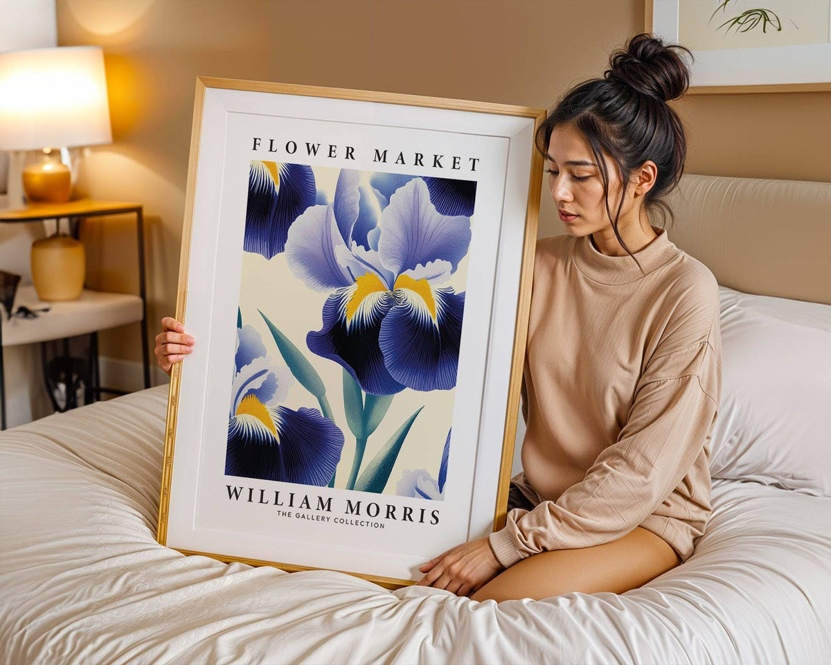 Framed print of purple flower wall art held by a person sitting on a bed with beige walls