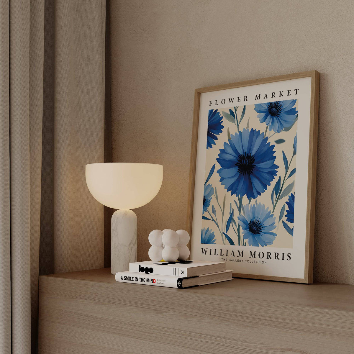 Botanical print leaning on a shelf with large blue flowers and white text next to a modern white lamp