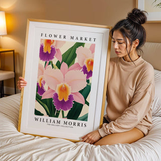 Framed print of a pink orchid flower illustration held by a woman sitting on a bed