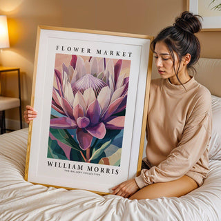 Framed Flower Wall Art of a king protea flower in pink and green tones held on a bed with a beige lamp