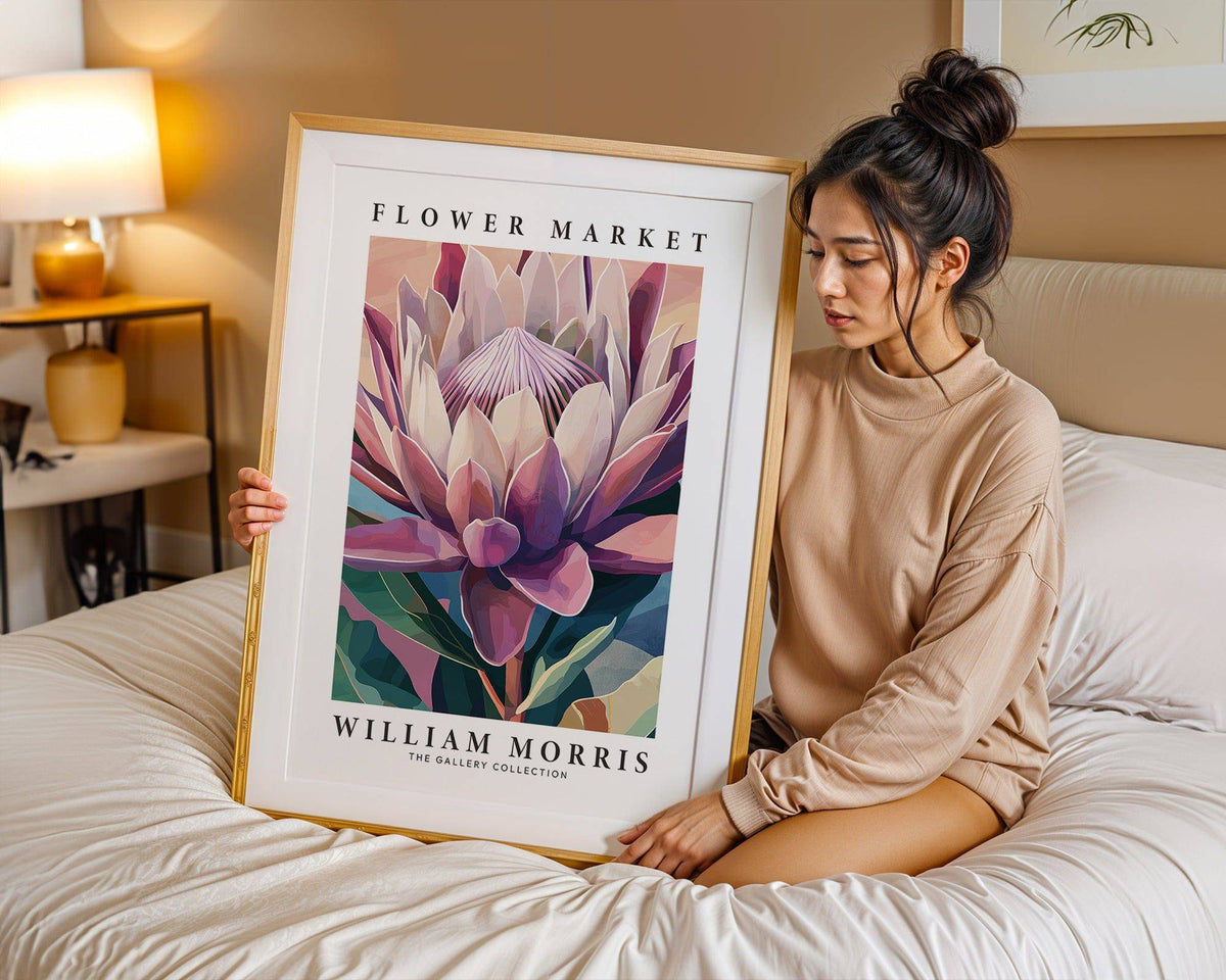 Framed Flower Wall Art of a king protea flower in pink and green tones held on a bed with a beige lamp