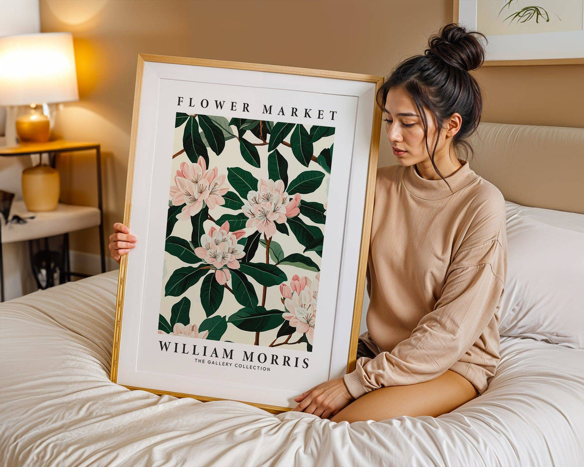 Framed Magnolia wall art showing pink magnolia flowers and green leaves held by a woman sitting on a bed