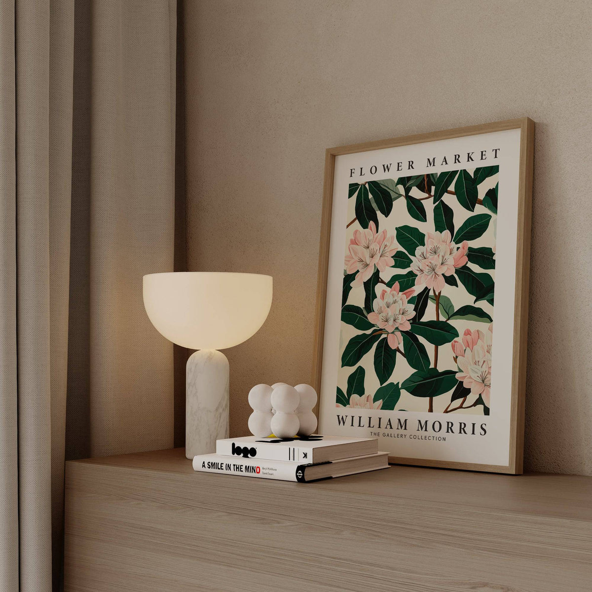 Framed Magnolia Wall Art with pink flowers and dark green leaves on a wooden surface with lamp and books