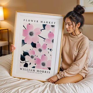 Framed print with pink dogwood flowers held by a woman sitting on a bed in a bedroom