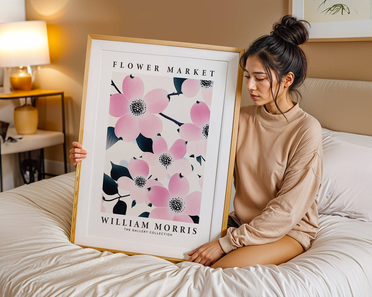 Framed print with pink dogwood flowers held by a woman sitting on a bed in a bedroom