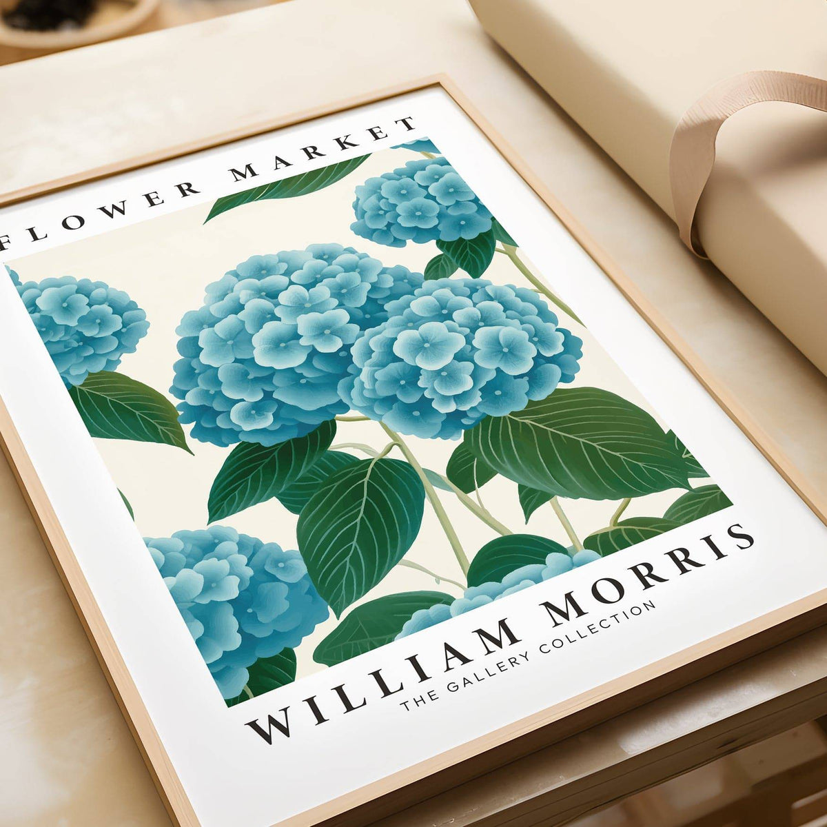 Framed Flower Market Prints showing blue hydrangea flowers and green leaves lying on a wooden surface next to pale wrapping paper