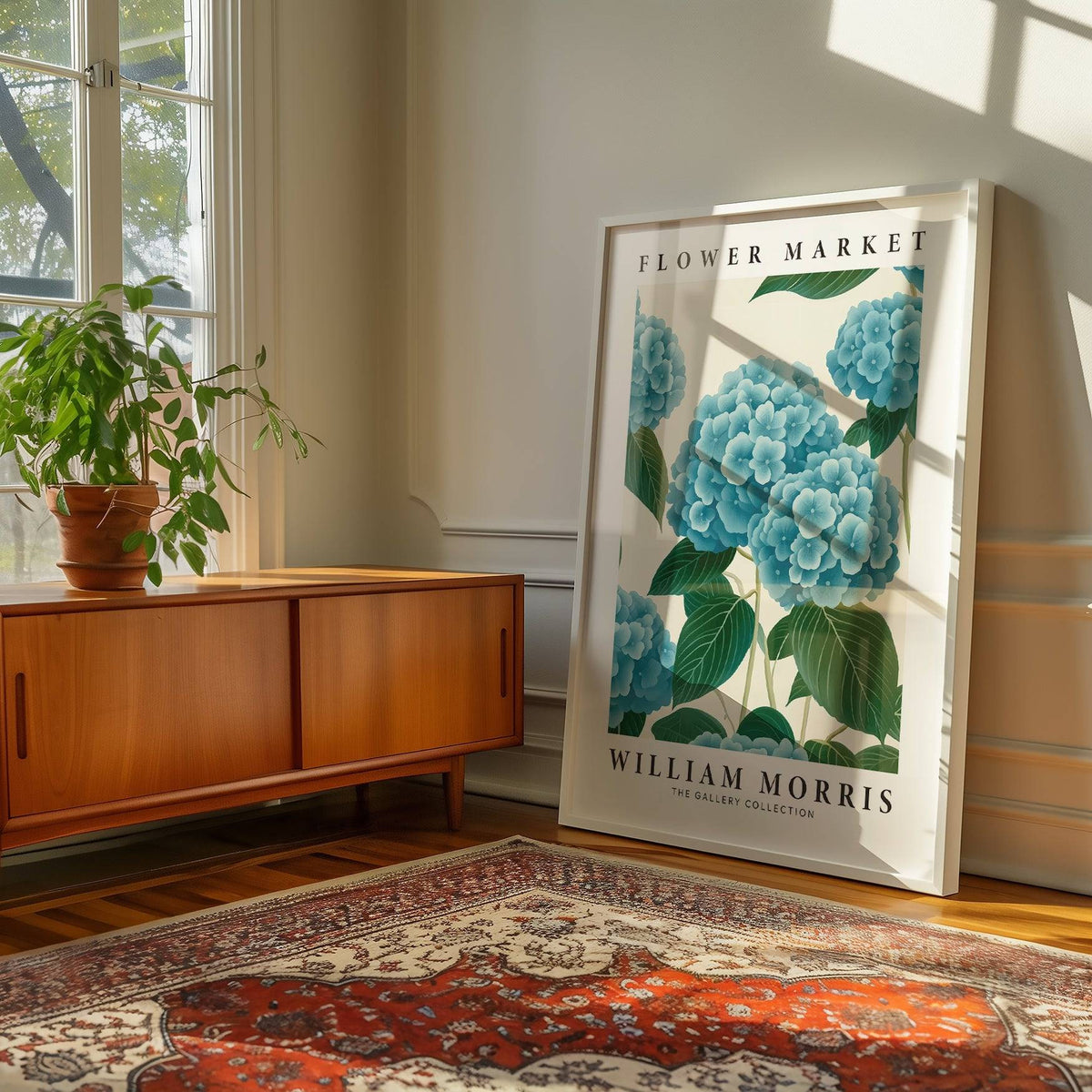 Print leaning on floor of blue hydrangea flowers in white frame with wooden sideboard and green plant nearby