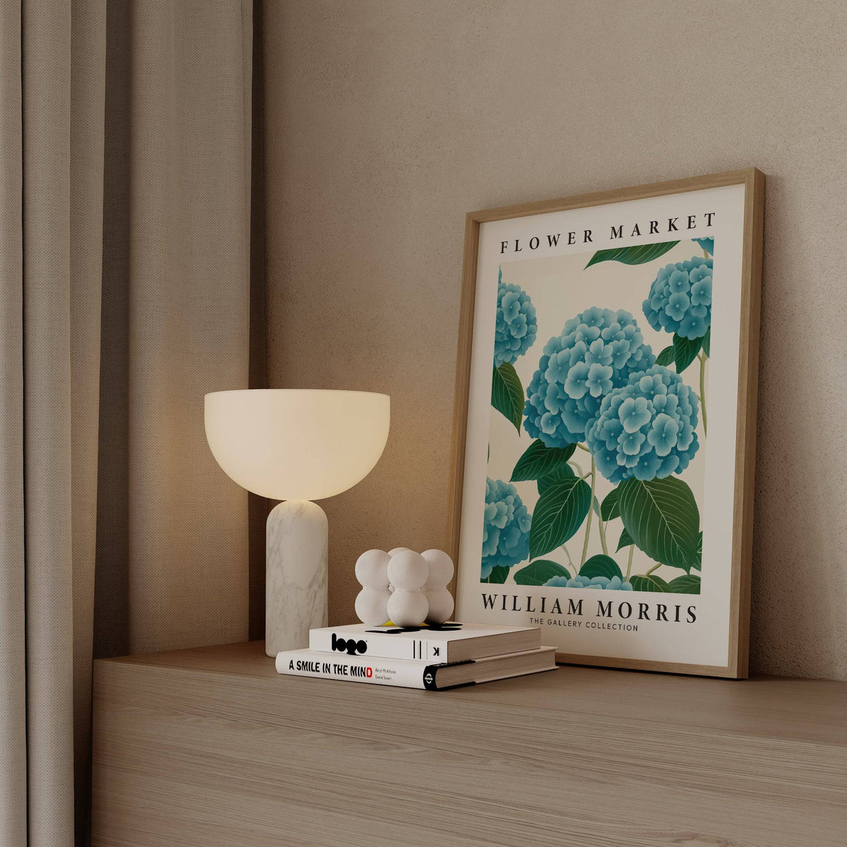 Flower Market Prints leaning print with blue hydrangea and green leaf illustration beside a modern lamp on a wooden surface
