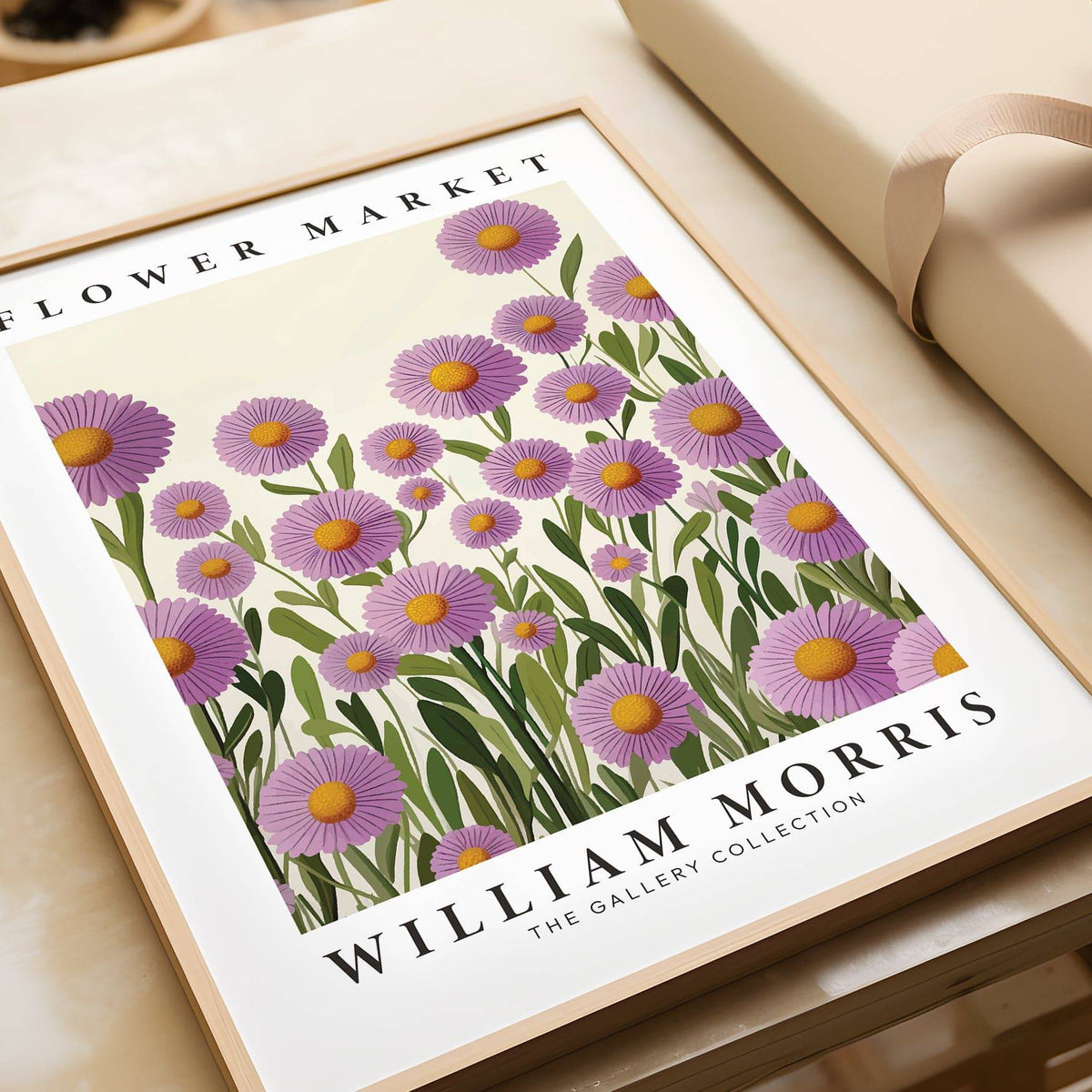 Framed purple floral wall art showing purple daisies with orange centres lying next to a beige gift box