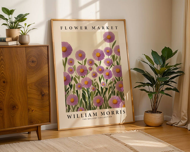 Print leaning on the floor of purple floral wall art with green leaves near a tall plant in a pot