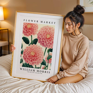 Framed wall art of pink dahlia flowers held by a woman on a bed with beige bedding