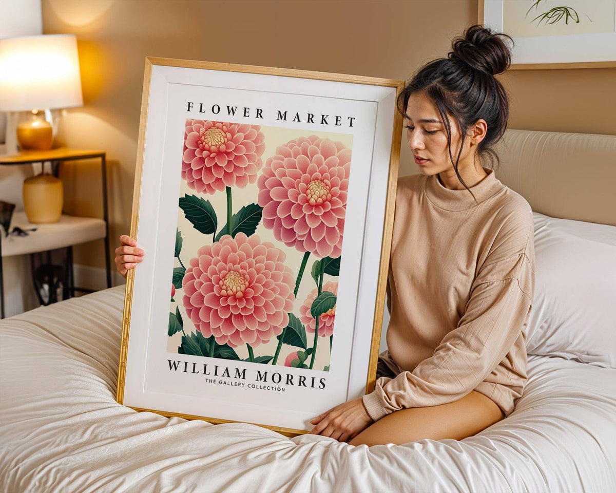 Framed wall art of pink dahlia flowers held by a woman on a bed with beige bedding