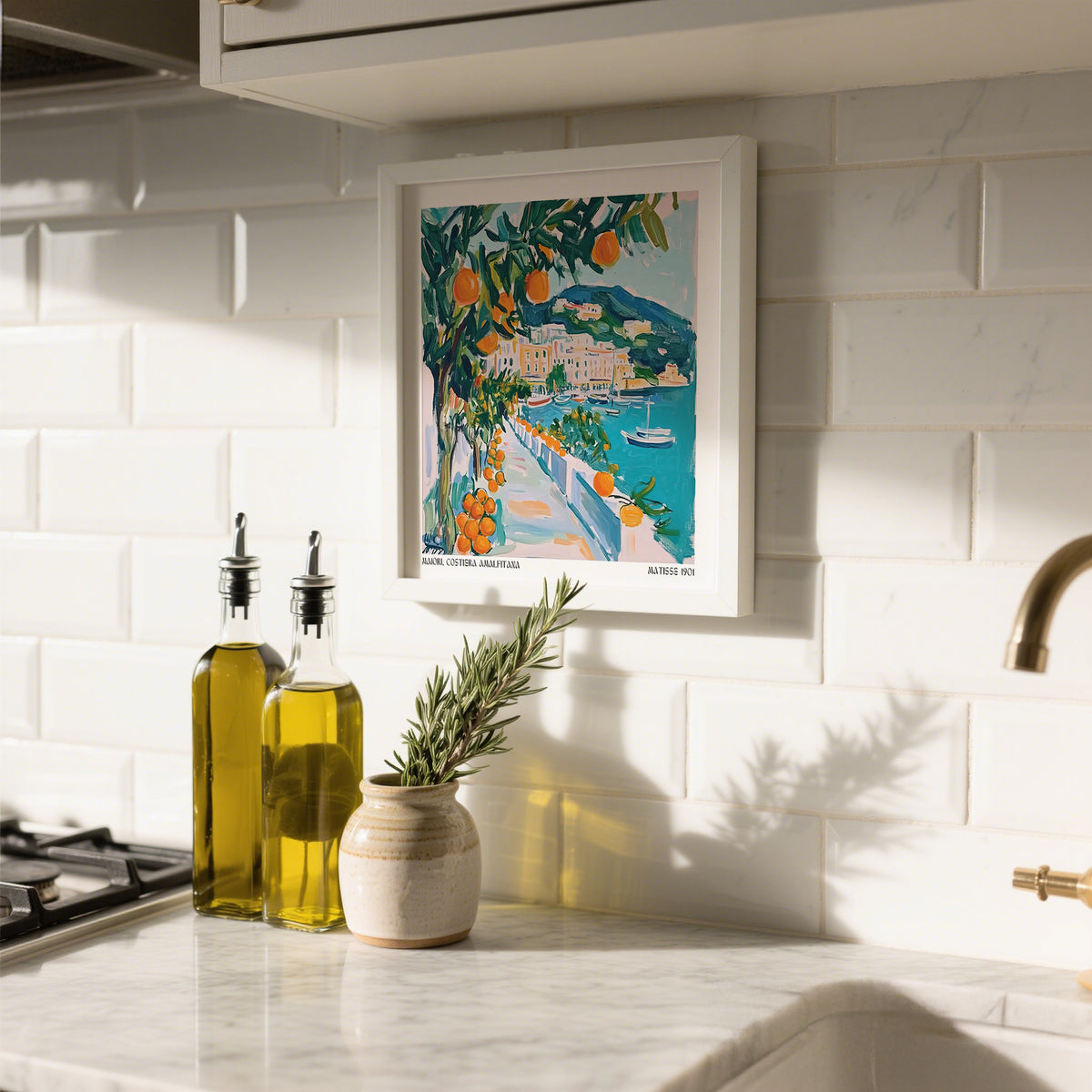 Art prints of Italy hanging in kitchen with orange tree illustration and seaside path near olive oil bottles