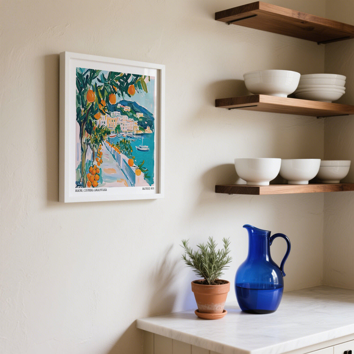 Print on a wall of orange tree by seaside path with blue sea and colourful buildings in a kitchen setting with shelves and crockery