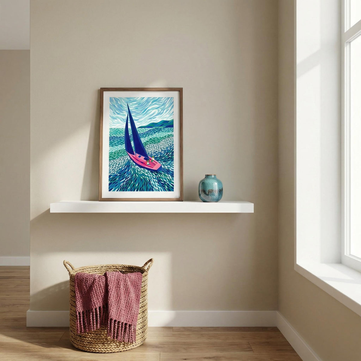 Print leaning on a shelf of sailboat art print with blue sails and a pink boat next to a blue vase