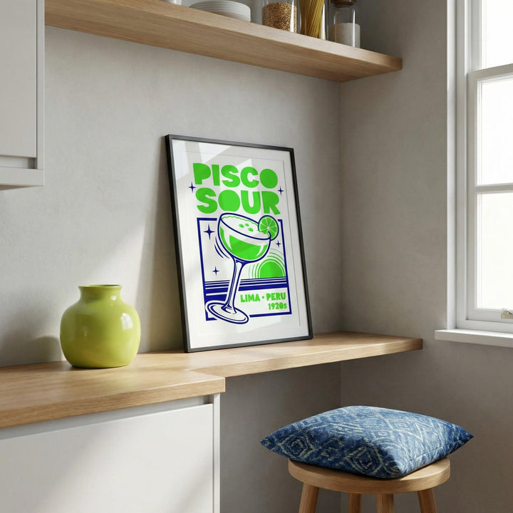 Print leaning on a wooden shelf of a green and blue Pisco Art cocktail poster with a green vase nearby