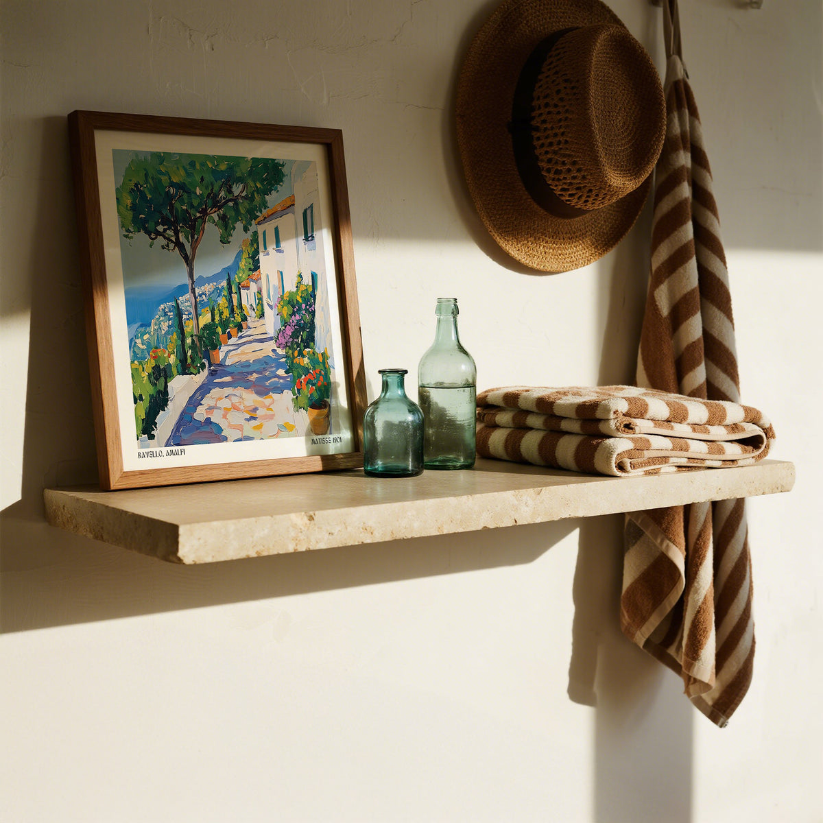 Prints of Amalfi Coast framed print leaning on a shelf with blue glass bottles and a straw hat