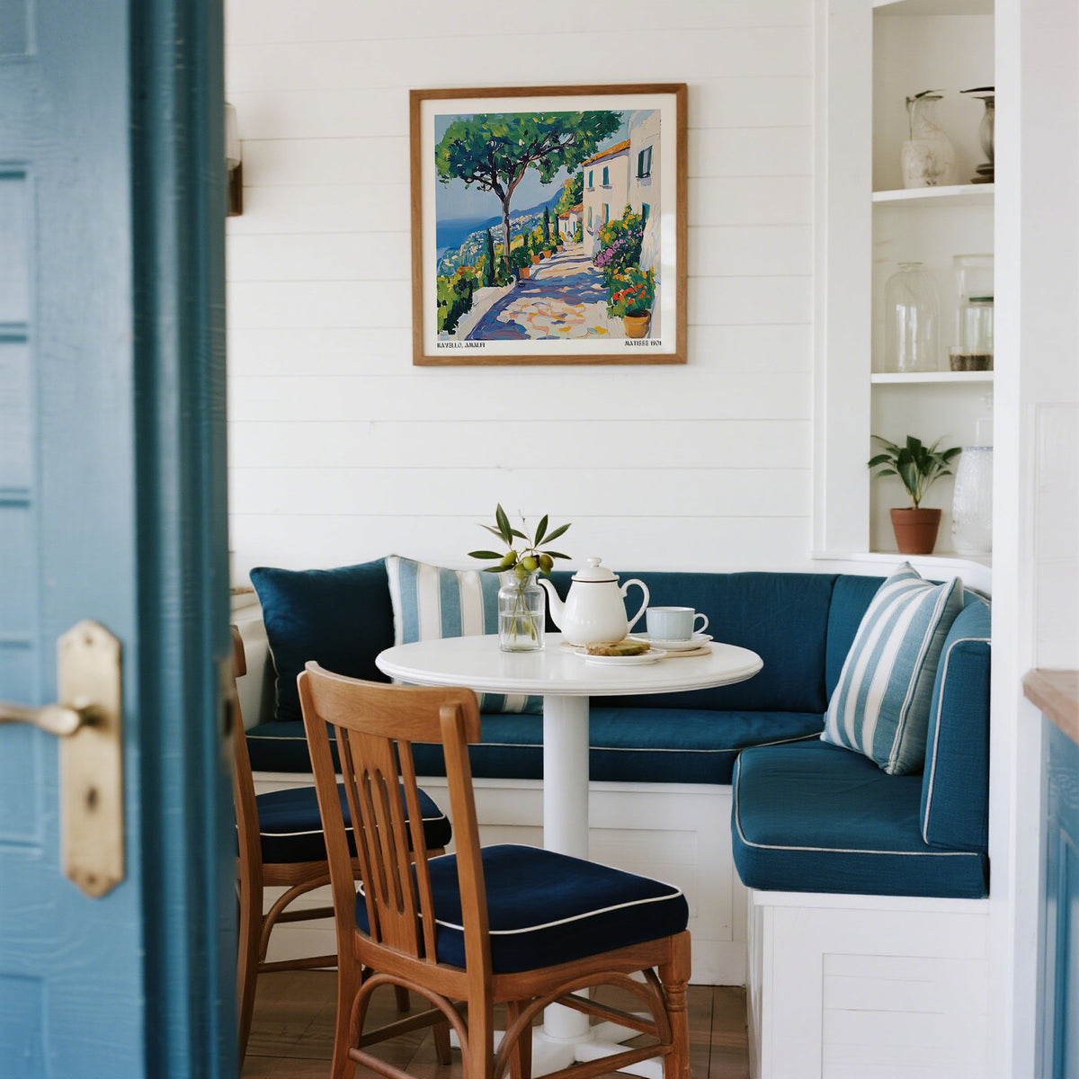 Prints of Amalfi Coast in a dining nook with blue cushioned bench and wooden chairs